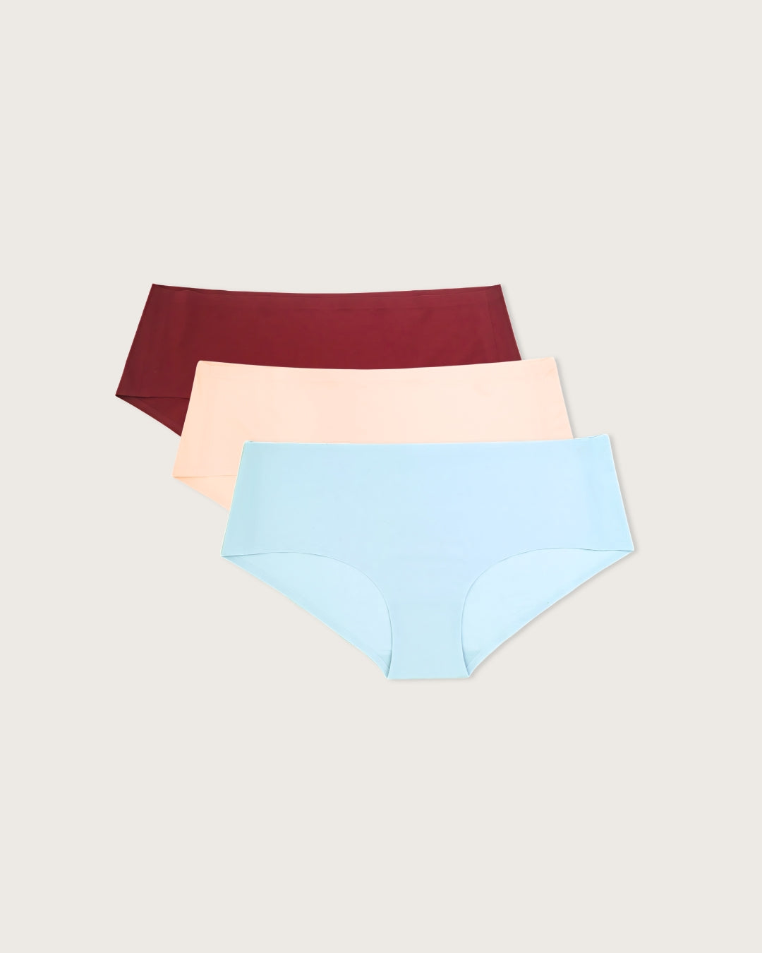 Three pairs of seamless underwear in burgundy, beige, and blue on a light gray background