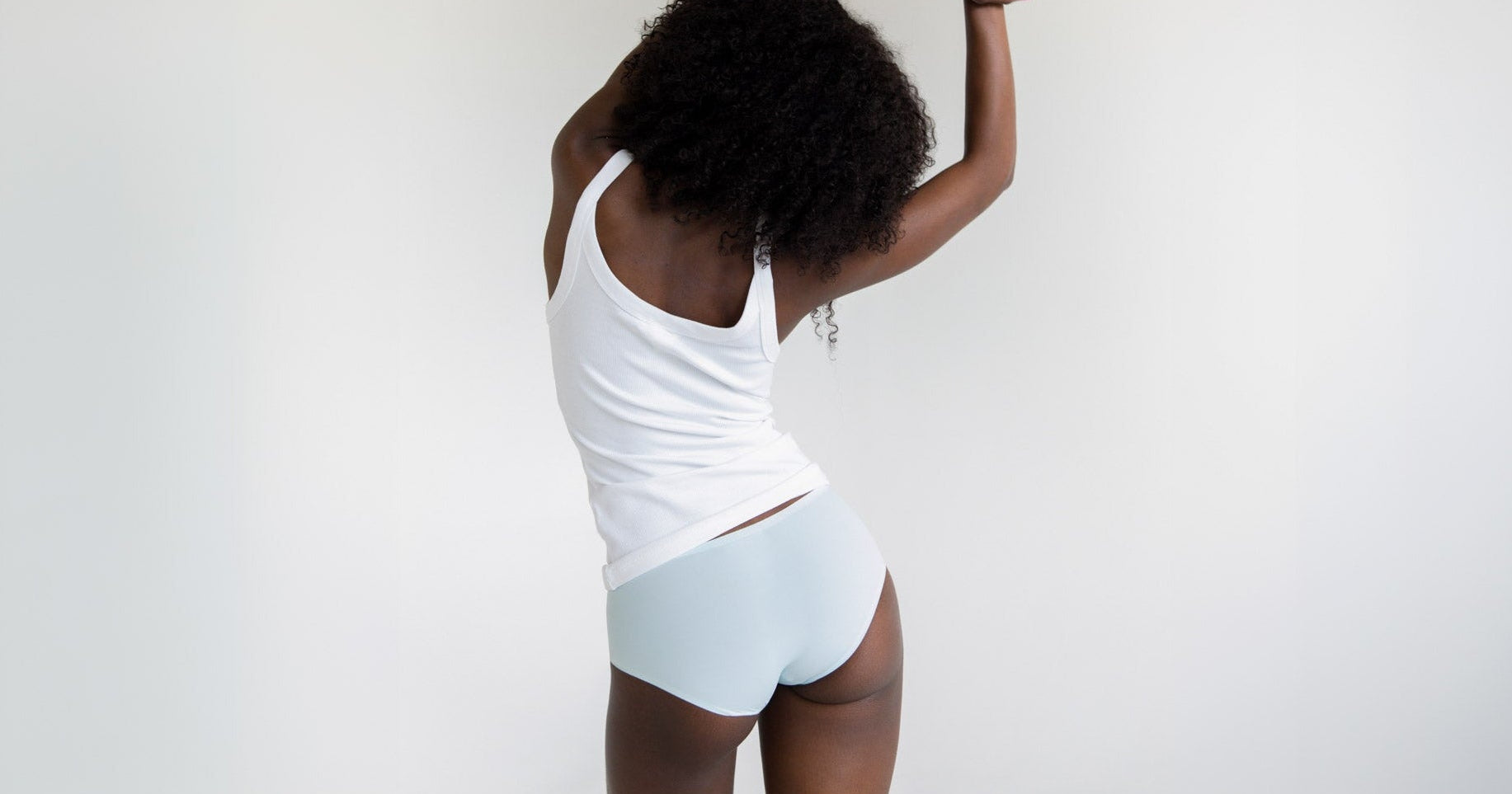 Woman wearing a white tank top and light blue seamless briefs that don't show underwear lines